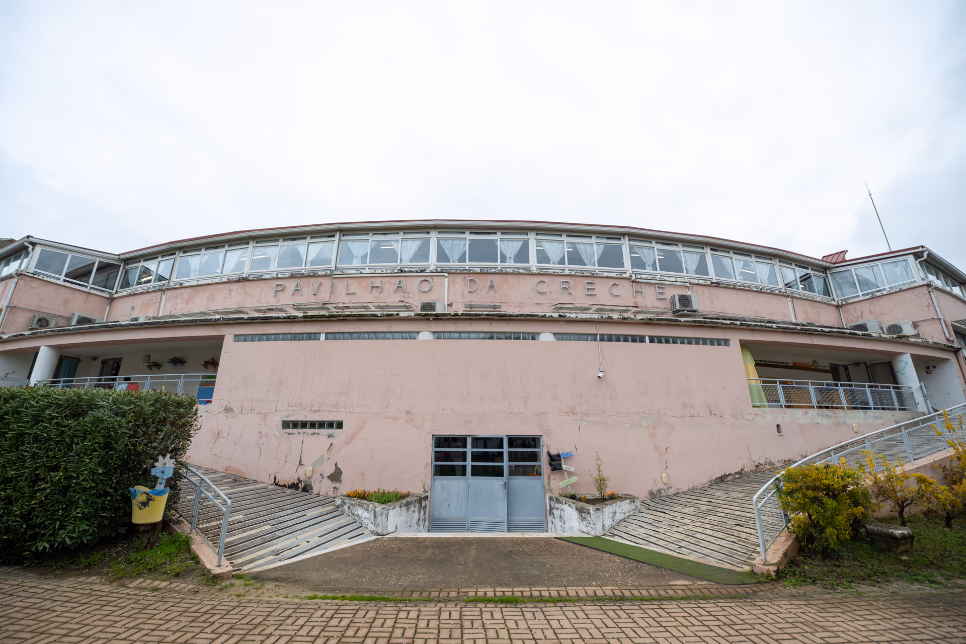Curved pink building with ramps on each side and sign reading Pavilhão da Creche.